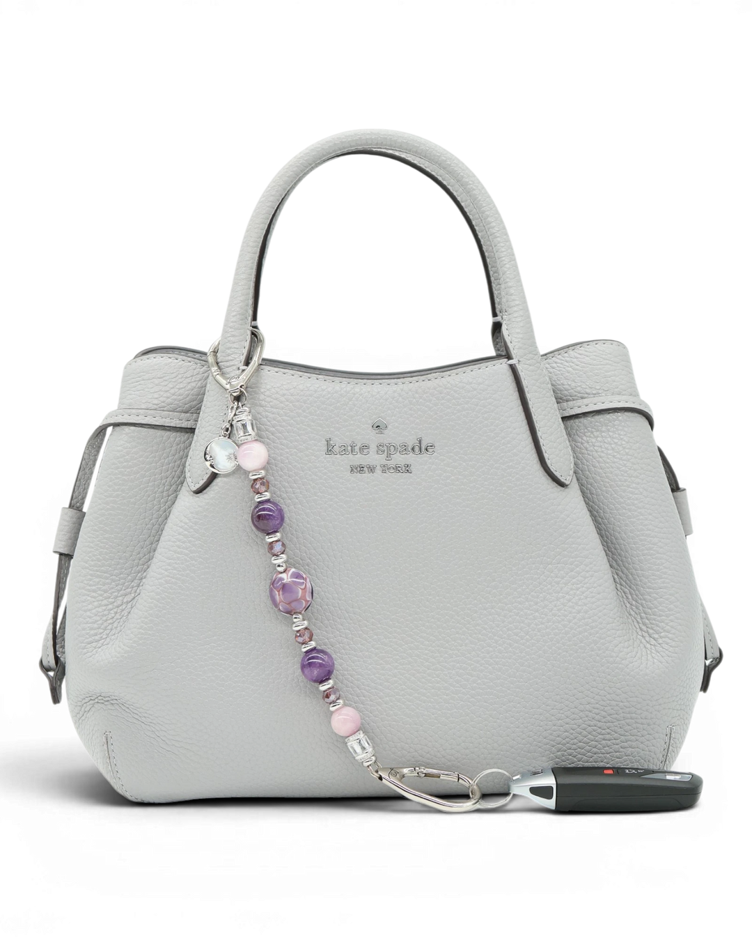LD Keyfinder Amethyst Moon beaded keychain with amethyst, kunzite, and artisan glass beads on a grey handbag.