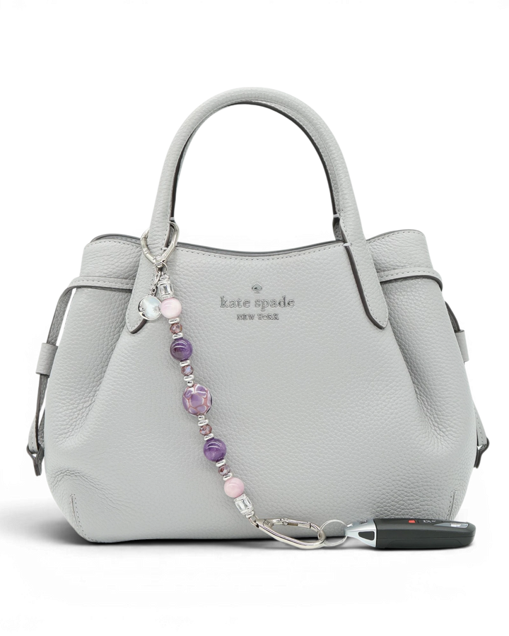 LD Keyfinder Amethyst Moon beaded keychain with amethyst, kunzite, and artisan glass beads on a grey handbag.