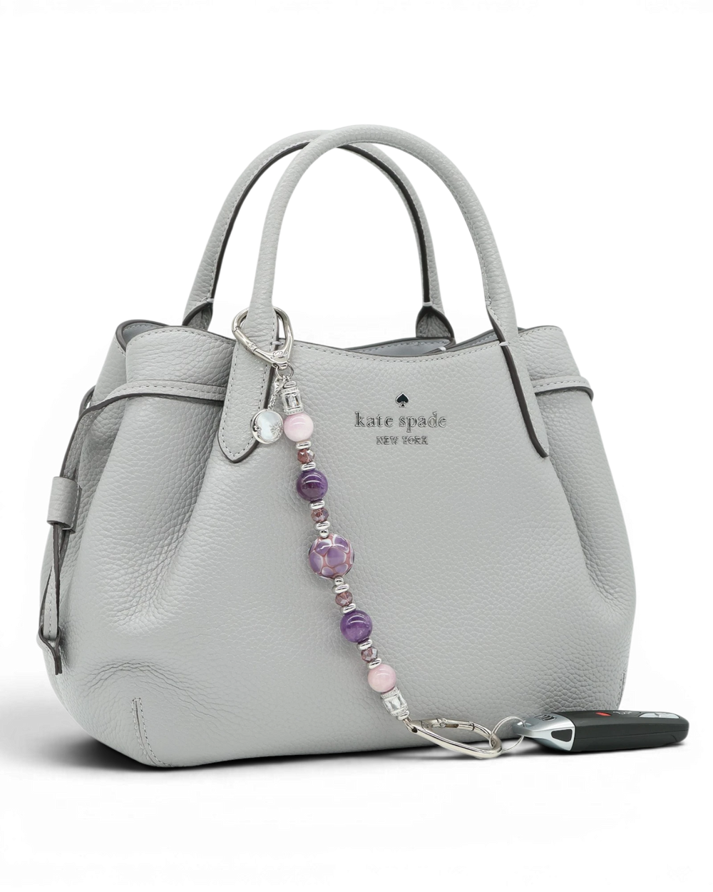 LD Keyfinder Amethyst Moon keychain with amethyst, kunzite, and glass beads, and a moon charm on a grey handbag.