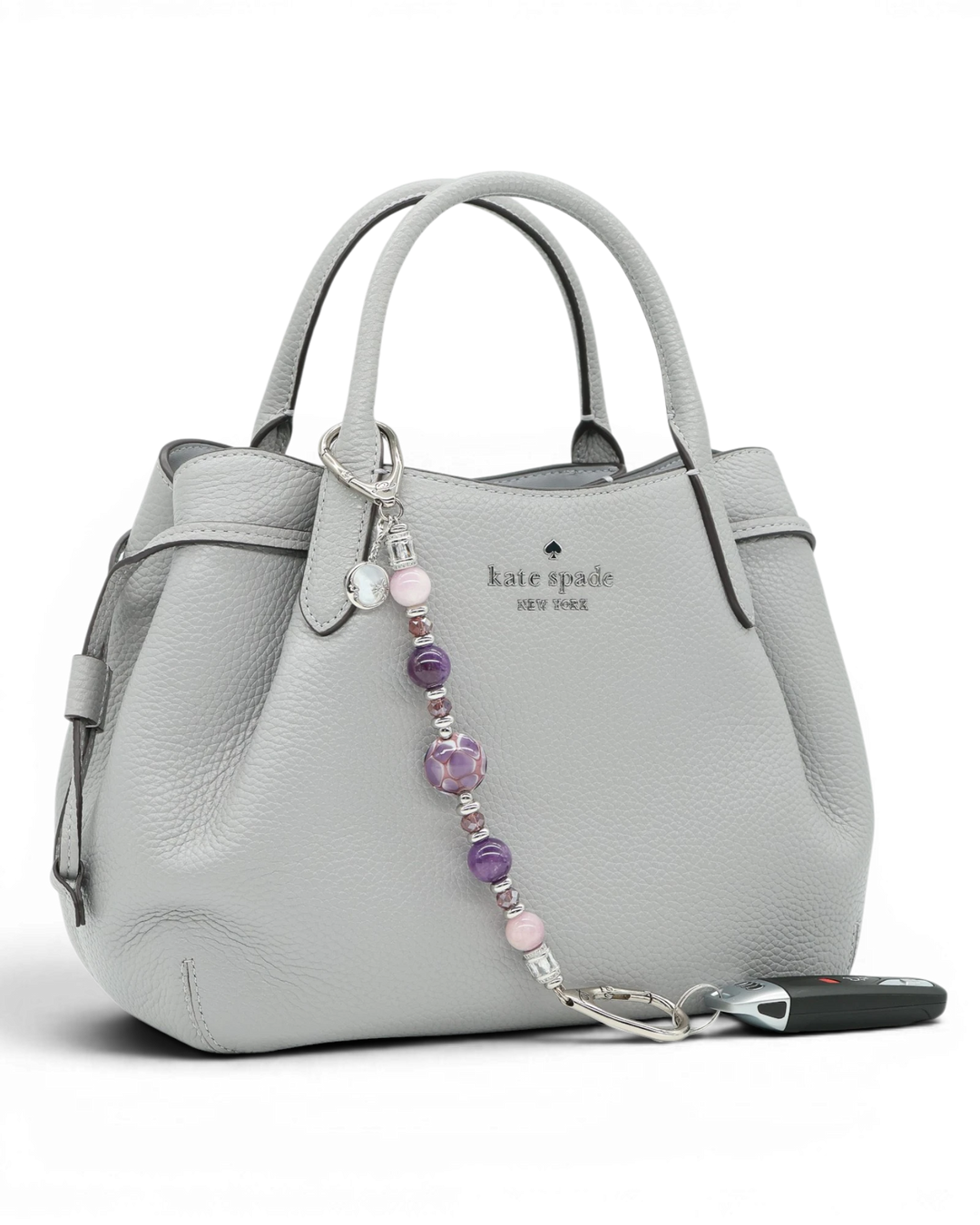 LD Keyfinder Amethyst Moon keychain with amethyst, kunzite, and glass beads, and a moon charm on a grey handbag.