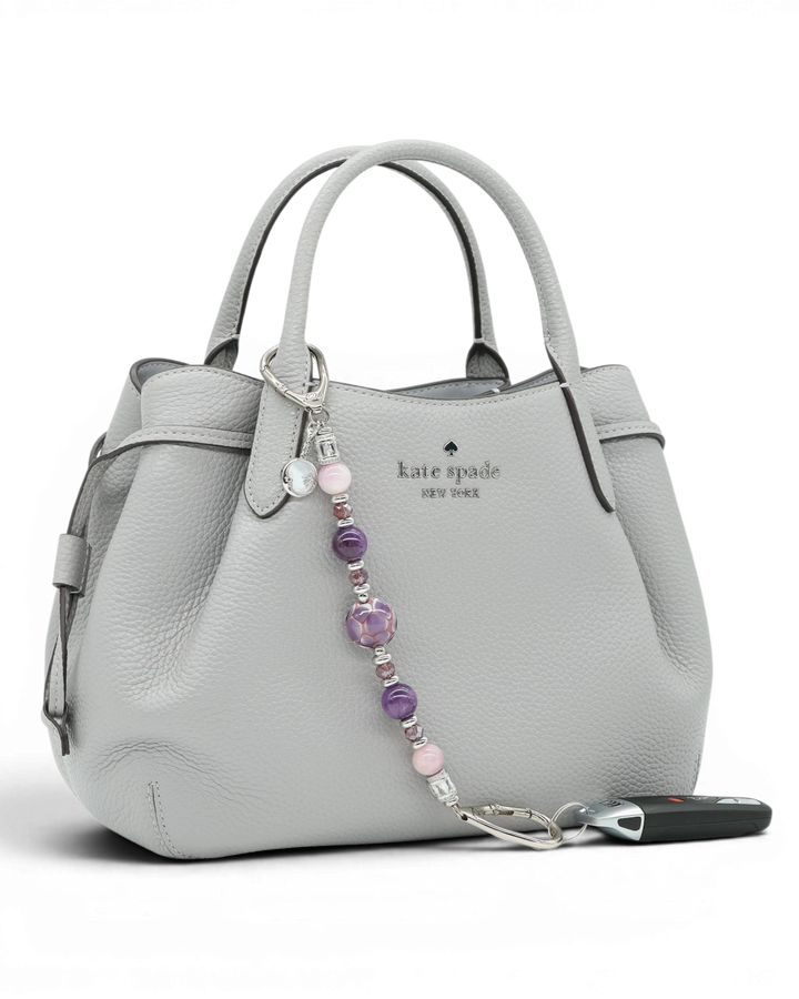 LD Keyfinder Amethyst Moon keychain with amethyst, kunzite, and glass beads, and a moon charm on a grey handbag.