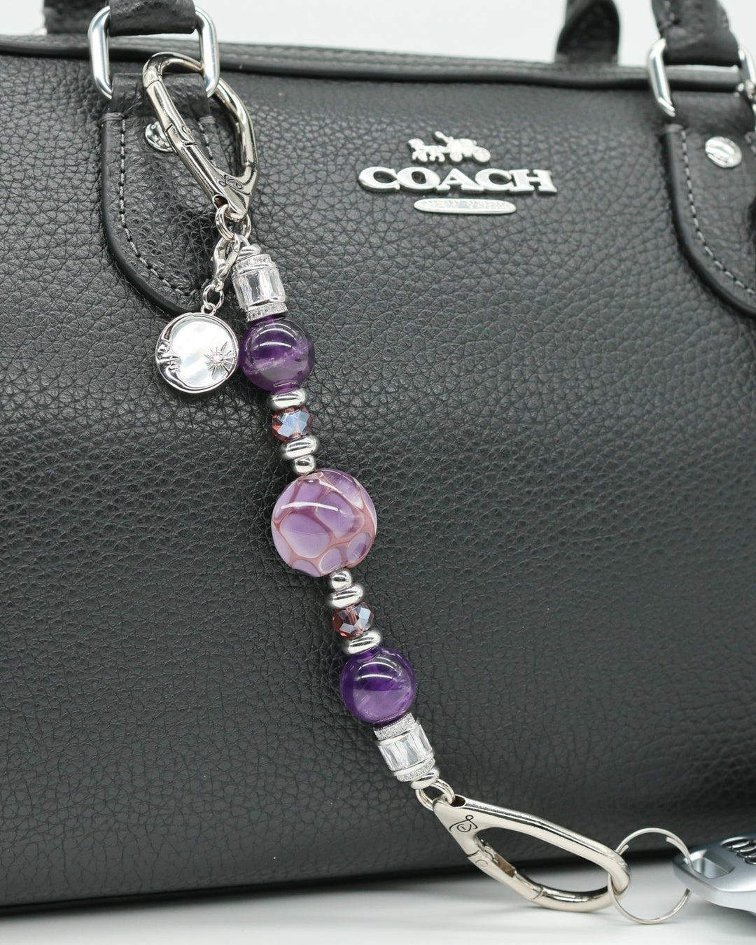 LD Keyfinder Petite Amethyst Moon charm with amethyst, glass beads, and moon charm on a black purse.