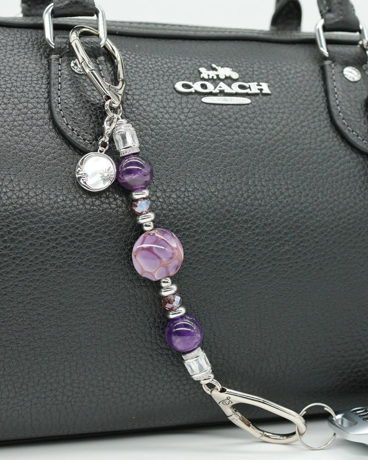 LD Keyfinder Petite Amethyst Moon charm with amethyst, glass beads, and moon charm on a black purse.