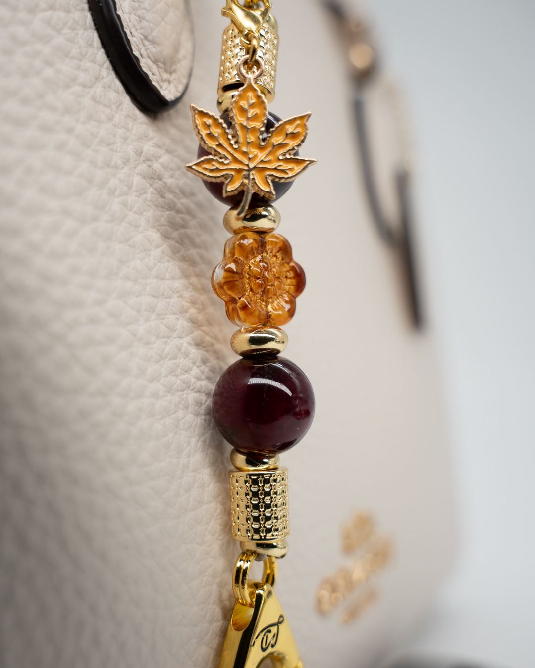 LD Keyfinder Hello Autumn-Mini featuring burgundy agate, amber glass flower, and gold maple leaf charm on a handbag.