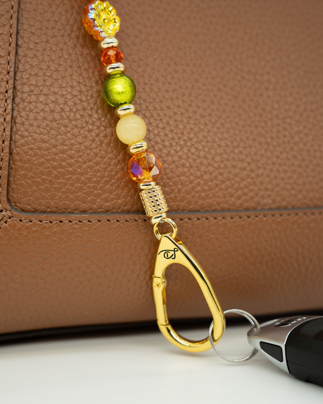 LD Keyfinder Autumn Festival beaded keychain with green foil, orange glass, and yellow jade beads on a brown handbag.