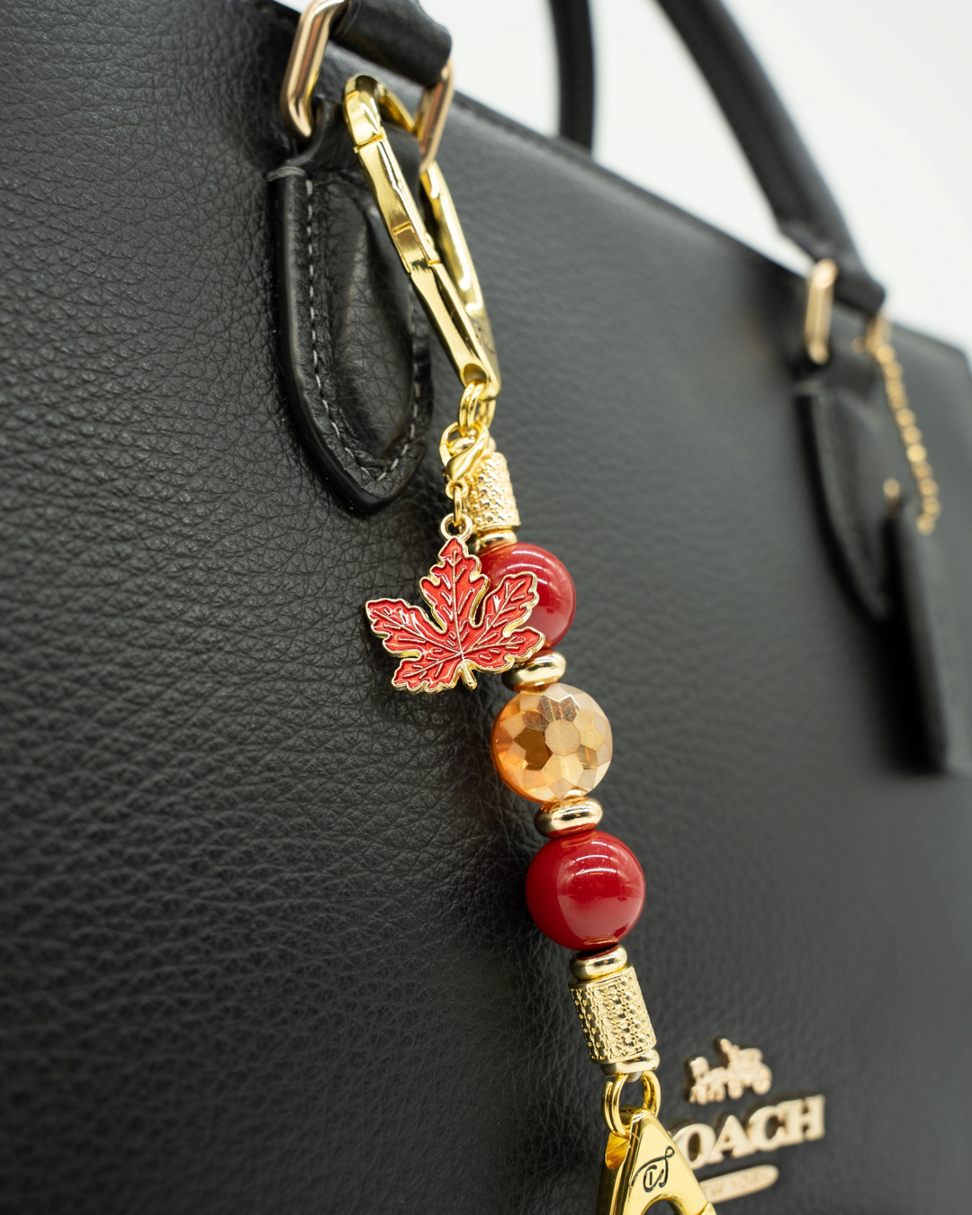 LD Keyfinder Autumn Glow-Mini bag charm with red shell pearls, amber glass bead, and gold maple leaf on black handbag
