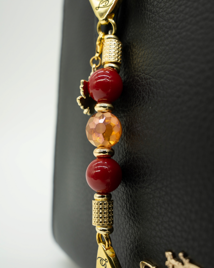 LD Keyfinder Autumn Glow-Mini featuring red shell pearls, etched amber glass, and a gold maple leaf charm on a bag.