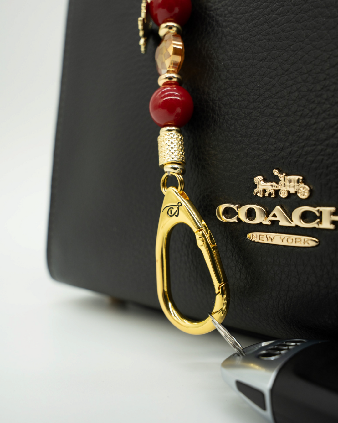 LD Keyfinder Autumn Glow-Mini featuring red shell pearls, amber glass bead, and gold maple leaf charm on a black bag