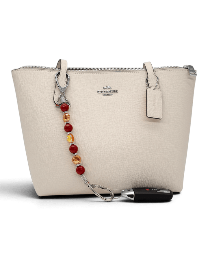 LD Keyfinder Autumn Whispers beaded accessory with red pearls, orange glass flowers, and charms attached to a handbag.