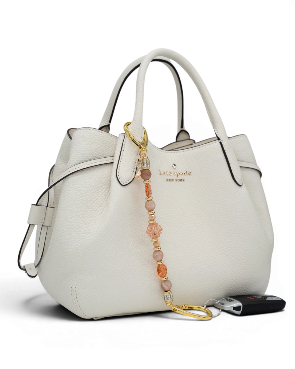 LD Keyfinder Birdsong Bliss beaded accessory with sunstone, coral flower, and gold bird charm attached to a white handbag.