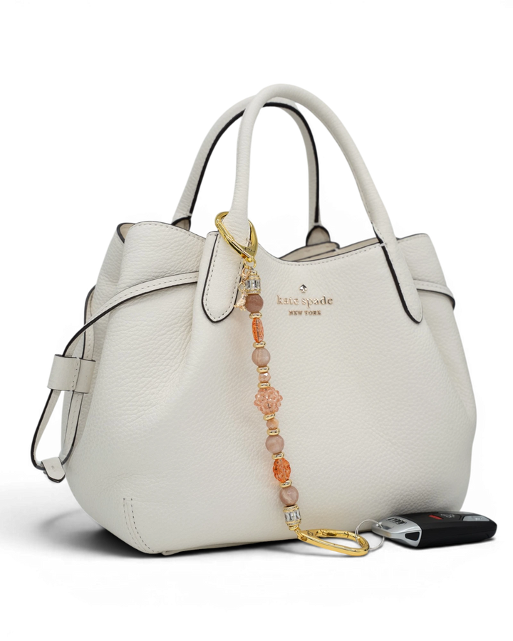 LD Keyfinder Birdsong Bliss beaded accessory with sunstone, coral flower, and gold bird charm attached to a white handbag.