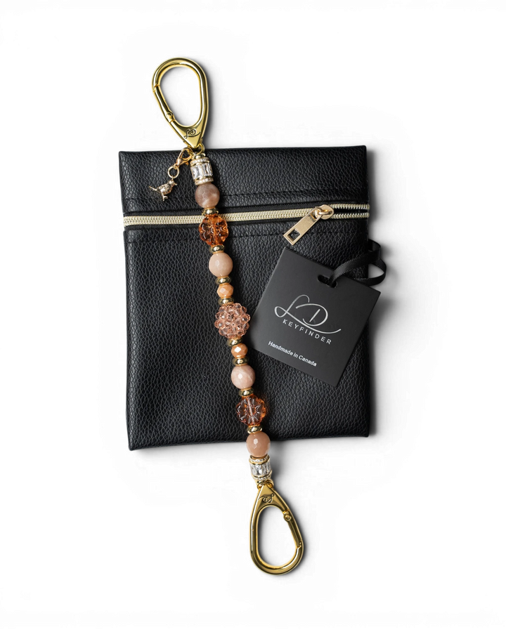 LD Keyfinder Birdsong Bliss beaded keychain with sunstone, peach glass, and gold-plated bird charm on a black pouch.