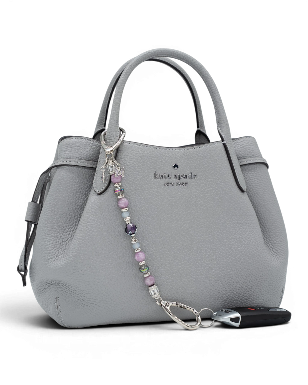LD Keyfinder Blooming Joy beaded accessory with lavender lepidolite and glass charms attached to a grey leather handbag