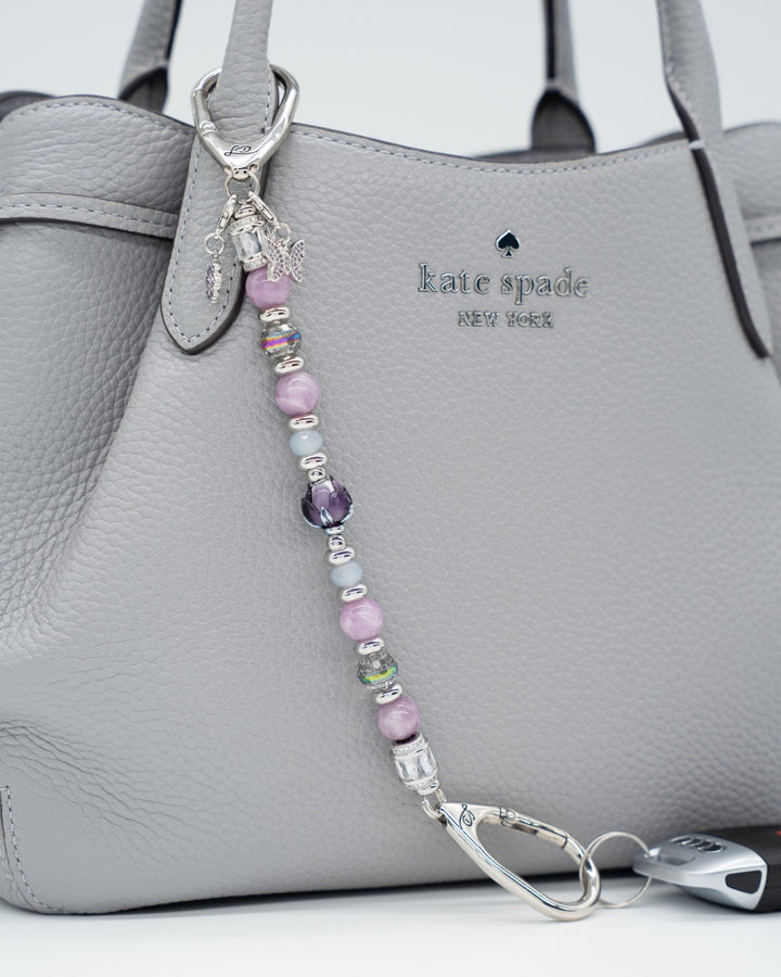 LD Keyfinder Blooming Joy beaded keychain with Lepidolite, purple Jade, and artisan glass tulip on a grey handbag.