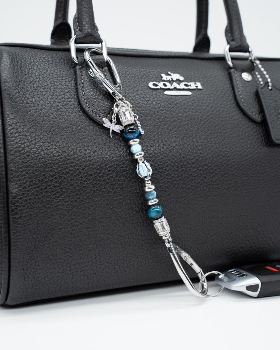 LD Keyfinder Petite Whispering Garden accessory with blue tiger eye, glass tulip, and dragonfly charm on a black bag.