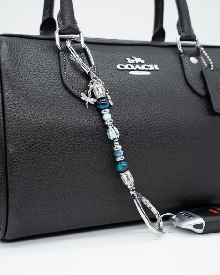 LD Keyfinder Petite Whispering Garden accessory with blue tiger eye, glass tulip, and dragonfly charm on a black bag.