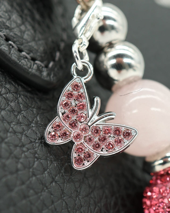 LD Keyfinder Blush Butterfly Mini charm with pink crystals, rose quartz, and silver beads on a black textured background.