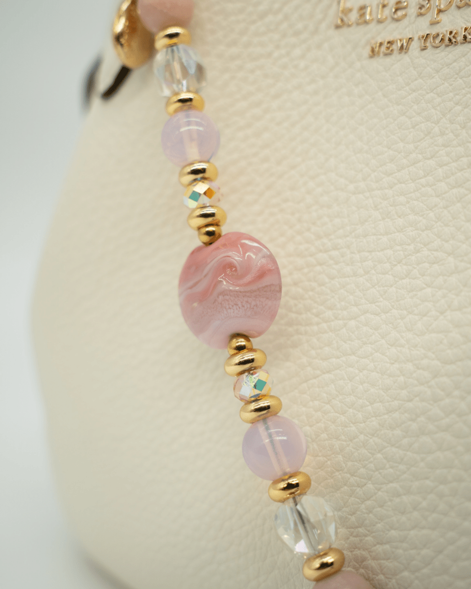 LD Keyfinder Blushing Opaline accessory with pink opal, artisan glass, and 18KT gold-plated beads on a cream handbag