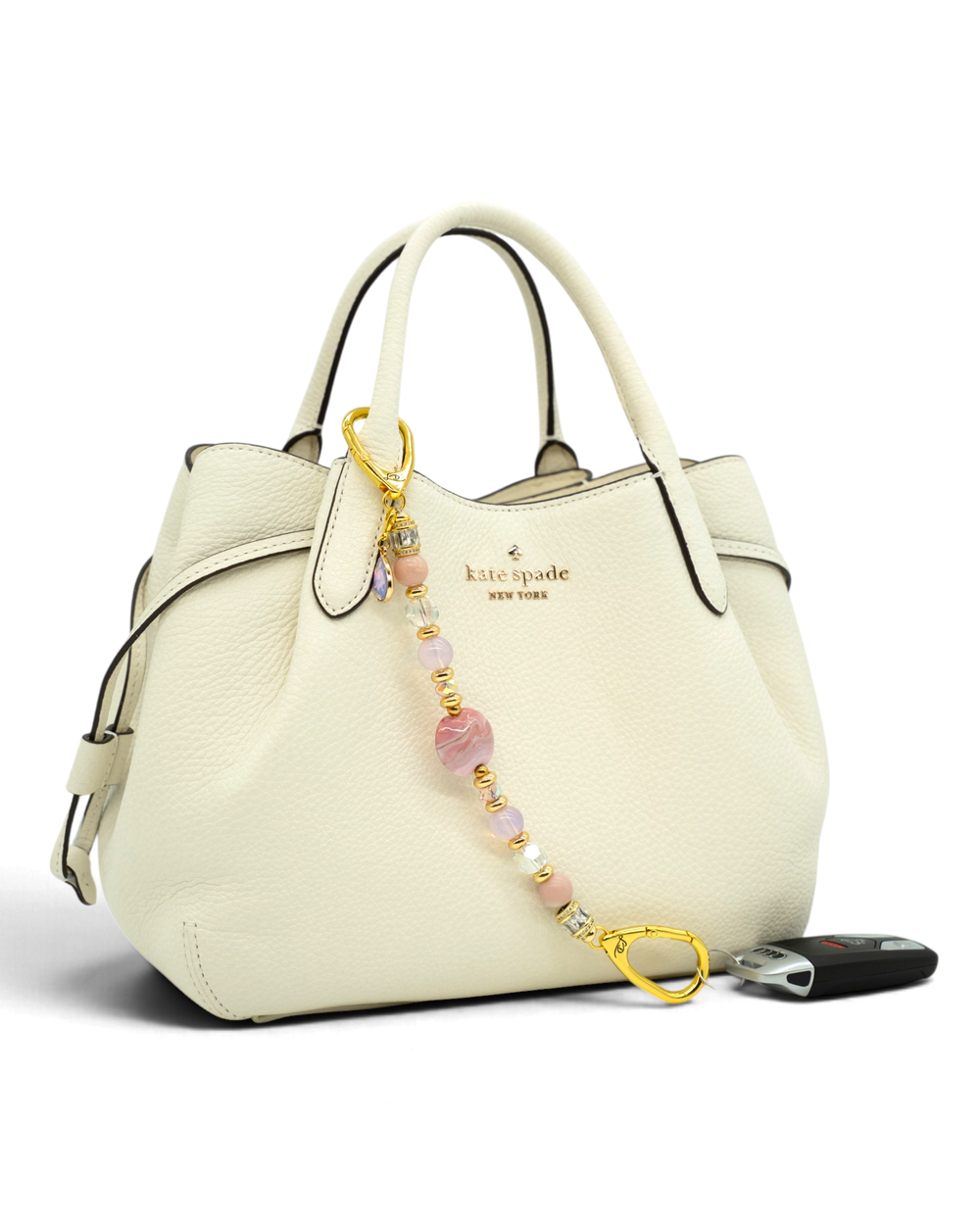 LD Keyfinder Blushing Opaline beaded accessory with pink opal and gold accents attached to a white leather handbag