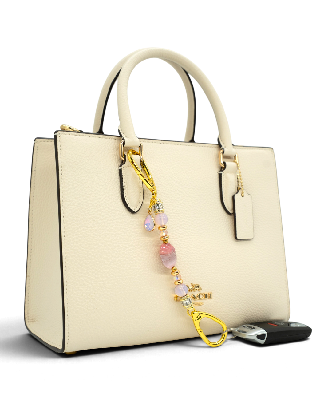 LD Keyfinder Blushing Opaline Petite accessory with pink opalite beads and gold accents attached to a cream handbag.