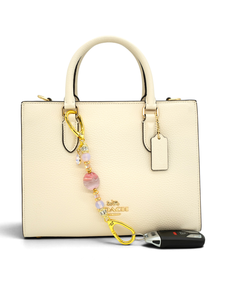 LD Keyfinder Blushing Opaline Petite accessory with pink opalite beads and gold accents attached to a cream handbag.