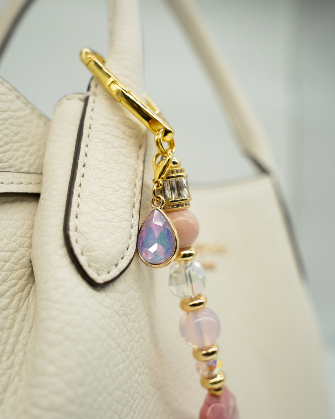 LD Keyfinder Blushing Opaline accessory with pink opal, gold accents, and a teardrop charm attached to a white bag.