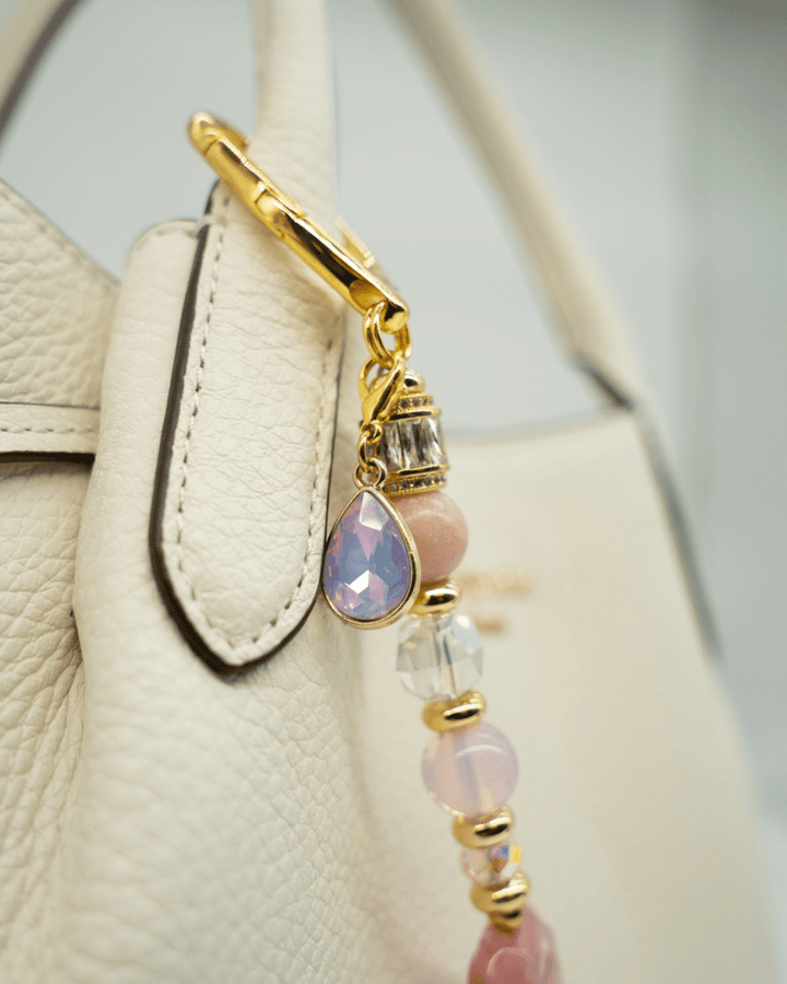 LD Keyfinder Blushing Opaline accessory with pink opal, gold accents, and a teardrop charm attached to a white bag.