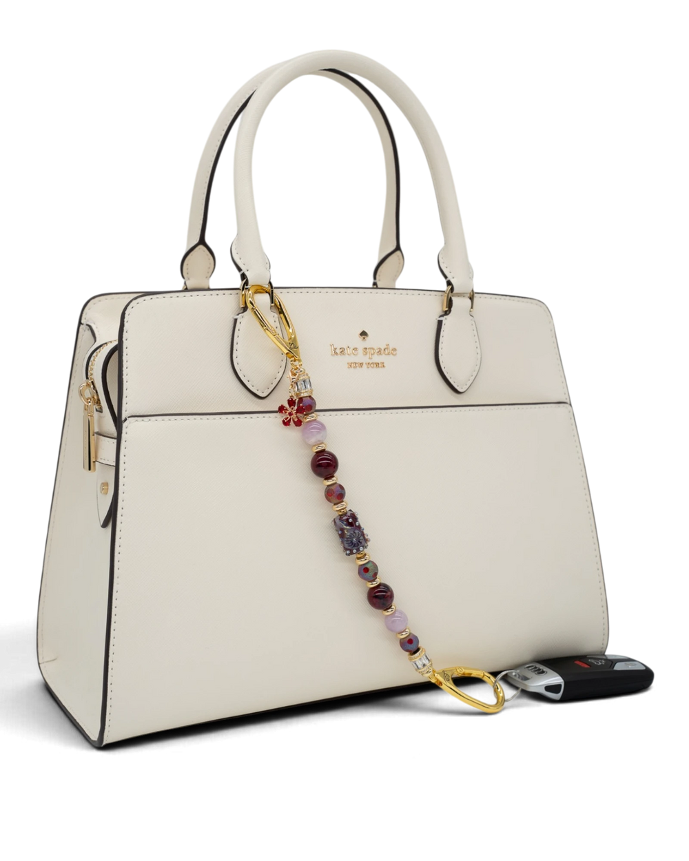 LD Keyfinder Bordeaux Bloom beaded accessory with burgundy agate, lavender kunzite, and gold flower charm on a handbag