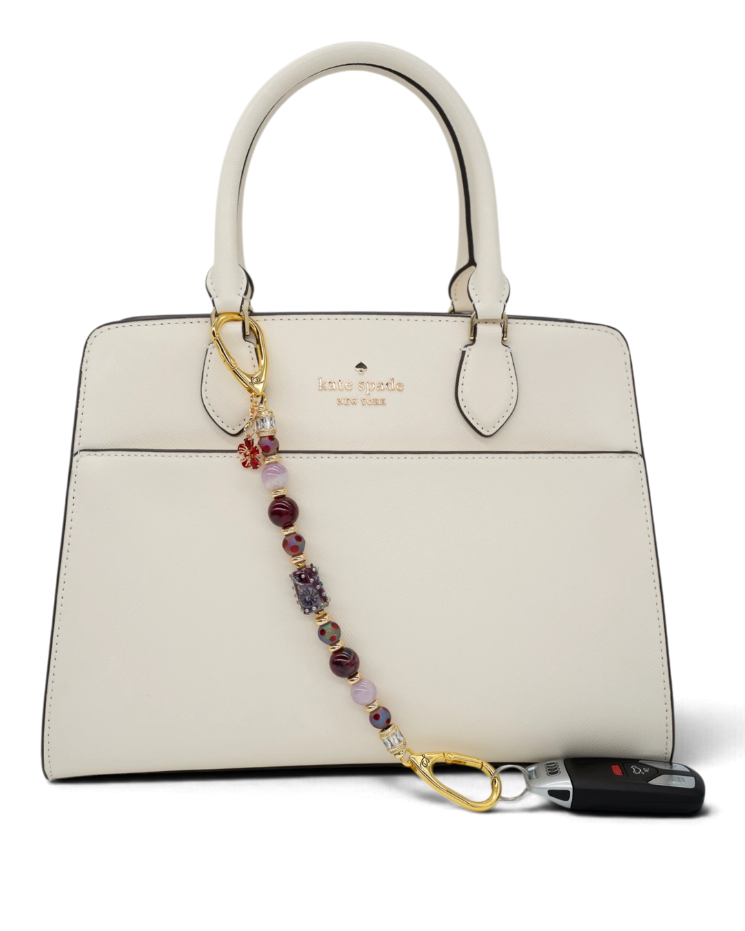 LD Keyfinder Bordeaux Bloom beaded accessory with burgundy agate, lavender kunzite, and gold-plated flower charm on a bag