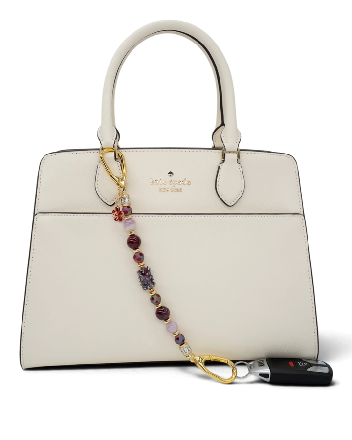 LD Keyfinder Bordeaux Bloom beaded accessory with burgundy agate, lavender kunzite, and gold-plated flower charm on a bag