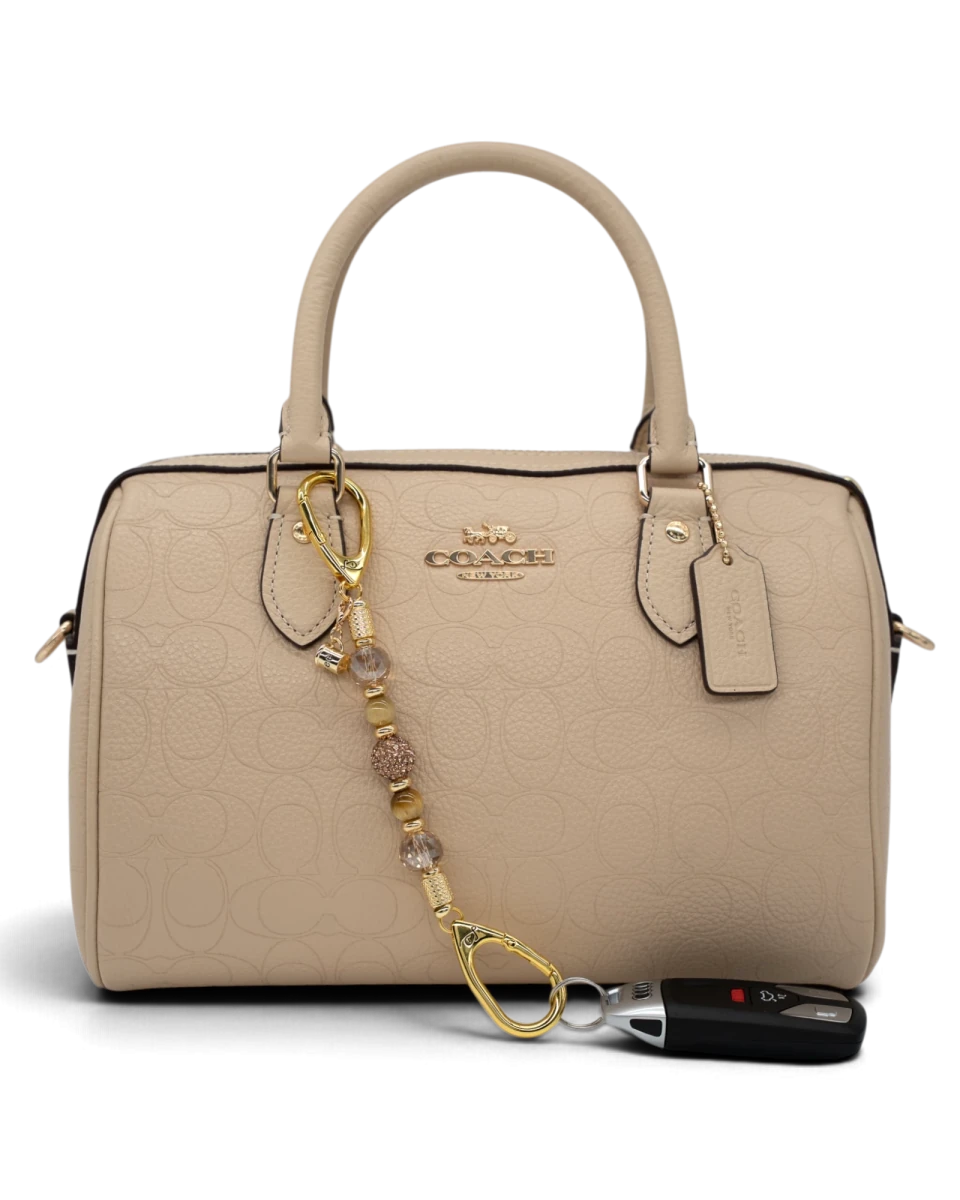 LD Keyfinder Caramel Latte-Mini beaded accessory with tiger eye and gold charms attached to a beige Coach handbag.