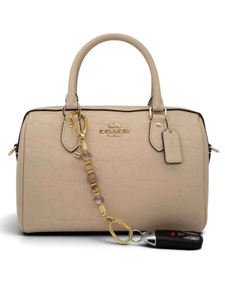 LD Keyfinder Caramel Latte-Mini beaded accessory with tiger eye and gold charms attached to a beige Coach handbag.