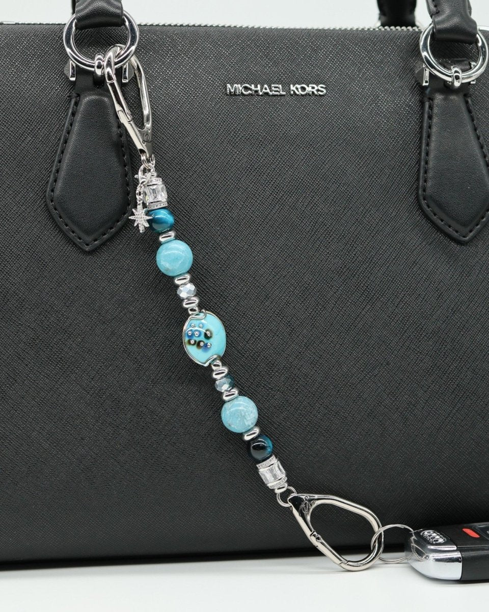 LD Keyfinder Celestial Tide charm with turquoise, aqua, blue tiger eye, larimar beads, silver accents, and star charm attached to a black handbag.