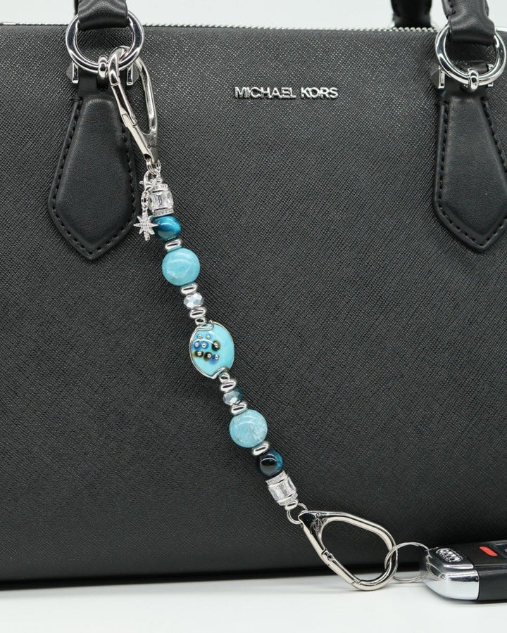 LD Keyfinder Celestial Tide charm with turquoise, aqua, blue tiger eye, larimar beads, silver accents, and star charm attached to a black handbag.