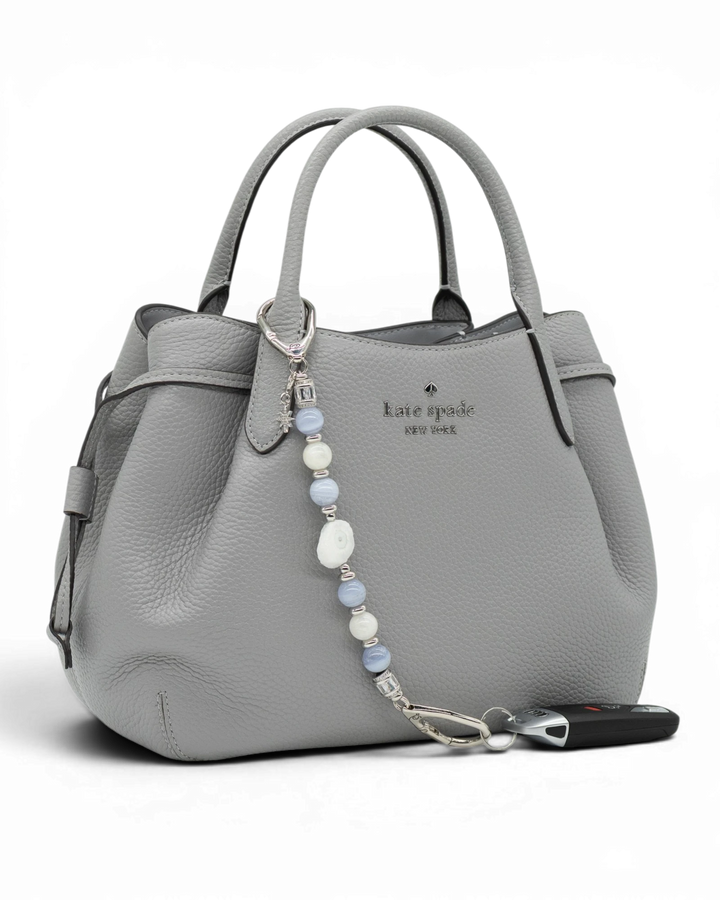 LD Keyfinder Cloud Dancer accessory with blue lace agate and moonstone beads attached to a grey leather handbag.
