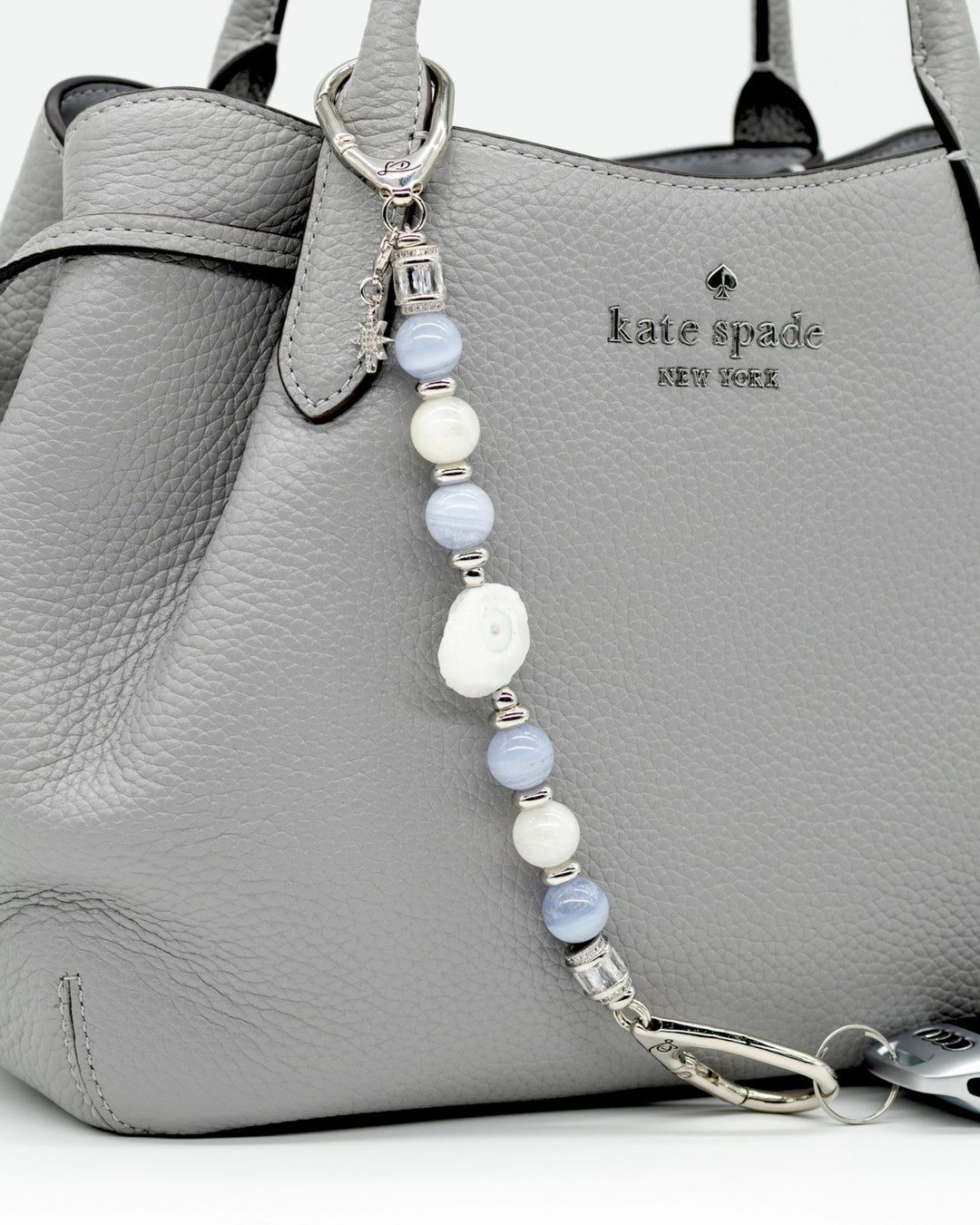 LD Keyfinder Cloud Dancer accessory with blue lace agate, moonstone, and a star charm attached to a grey handbag.