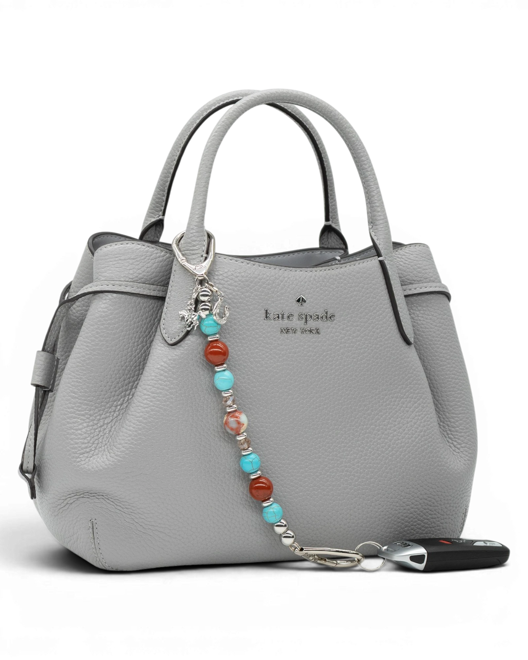 LD Keyfinder Cowgirl Dreams beaded keychain with turquoise, red jasper, and charms attached to a grey leather handbag.