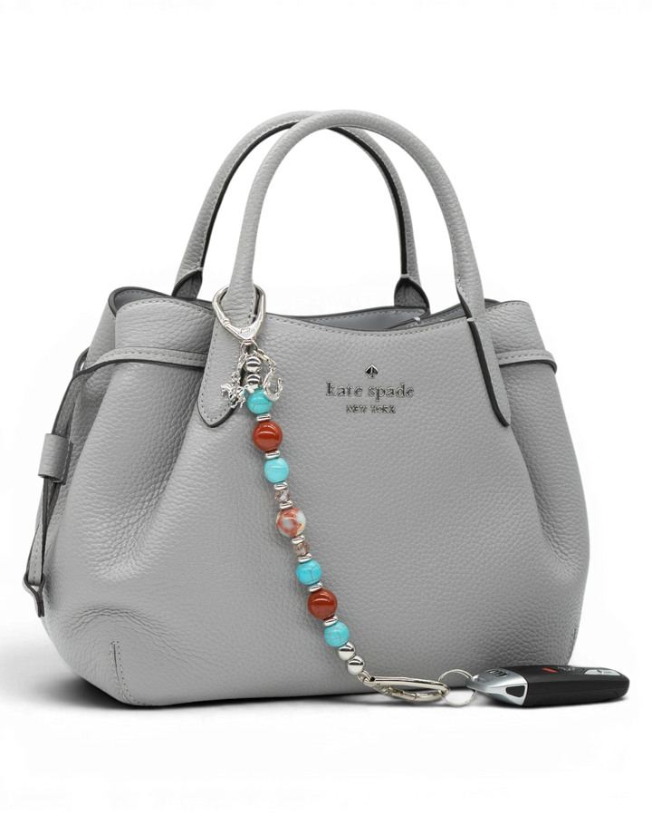 LD Keyfinder Cowgirl Dreams beaded keychain with turquoise, red jasper, and charms attached to a grey leather handbag.