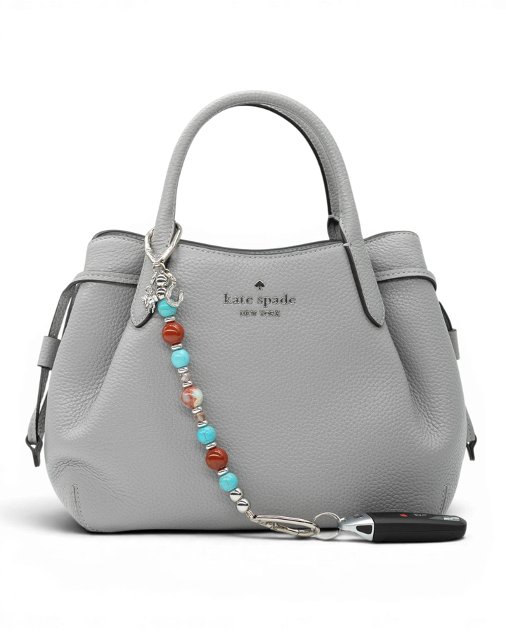 LD Keyfinder Cowgirl Dreams beaded accessory with red jasper, turquoise, and charms attached to a grey leather handbag.