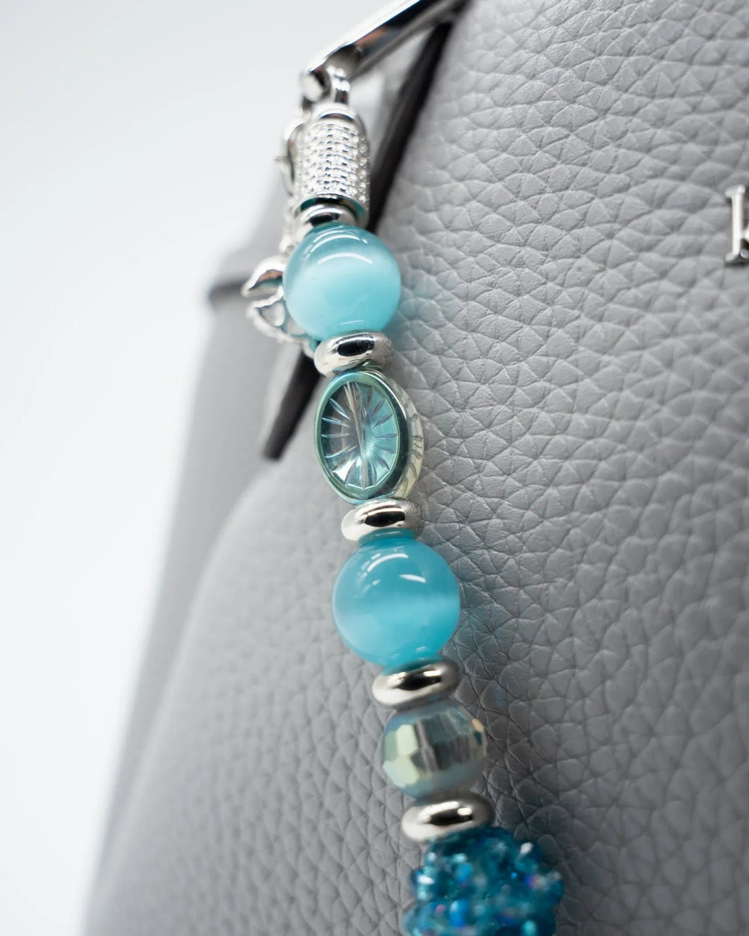 LD Keyfinder Dolphin Dream beaded accessory with aqua glass beads and a pavé rhinestone dolphin charm on a grey bag.