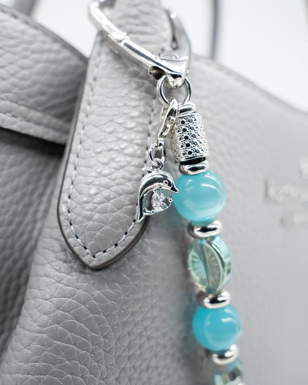 LD Keyfinder Dolphin Dream accessory with aqua beads and a rhinestone dolphin charm attached to a grey leather handbag.