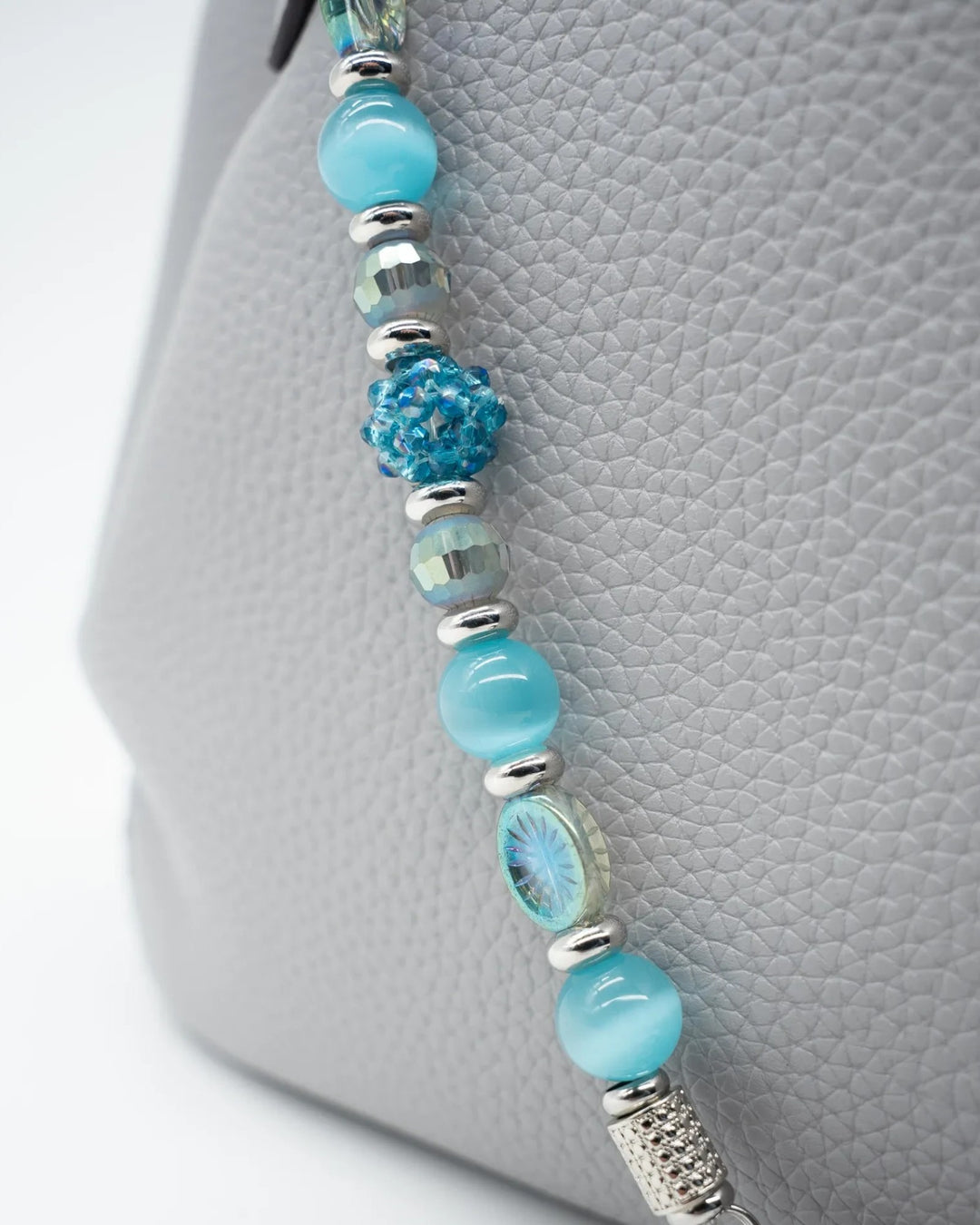 LD Keyfinder Dolphin Dream beaded accessory with aqua cat's eye, etched glass, and faceted beads on a grey handbag
