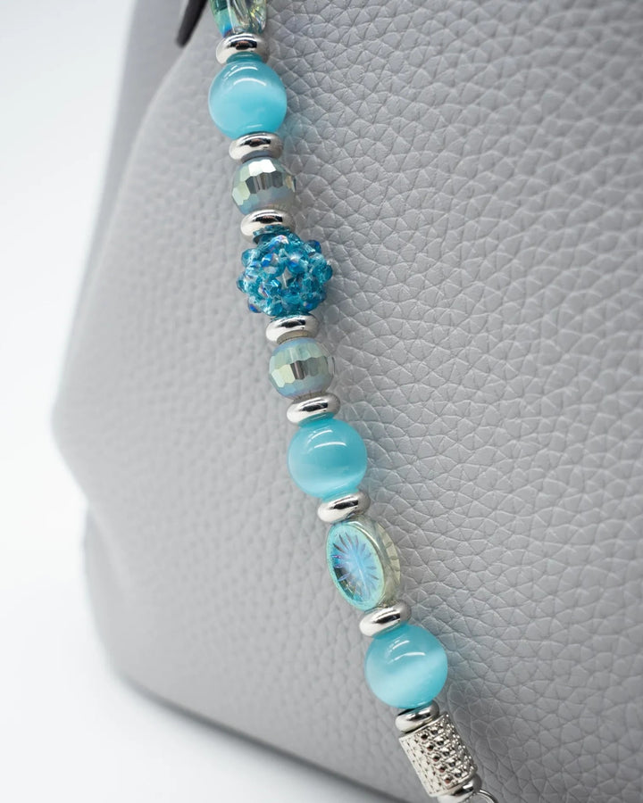 LD Keyfinder Dolphin Dream beaded accessory with aqua cat's eye, etched glass, and faceted beads on a grey handbag