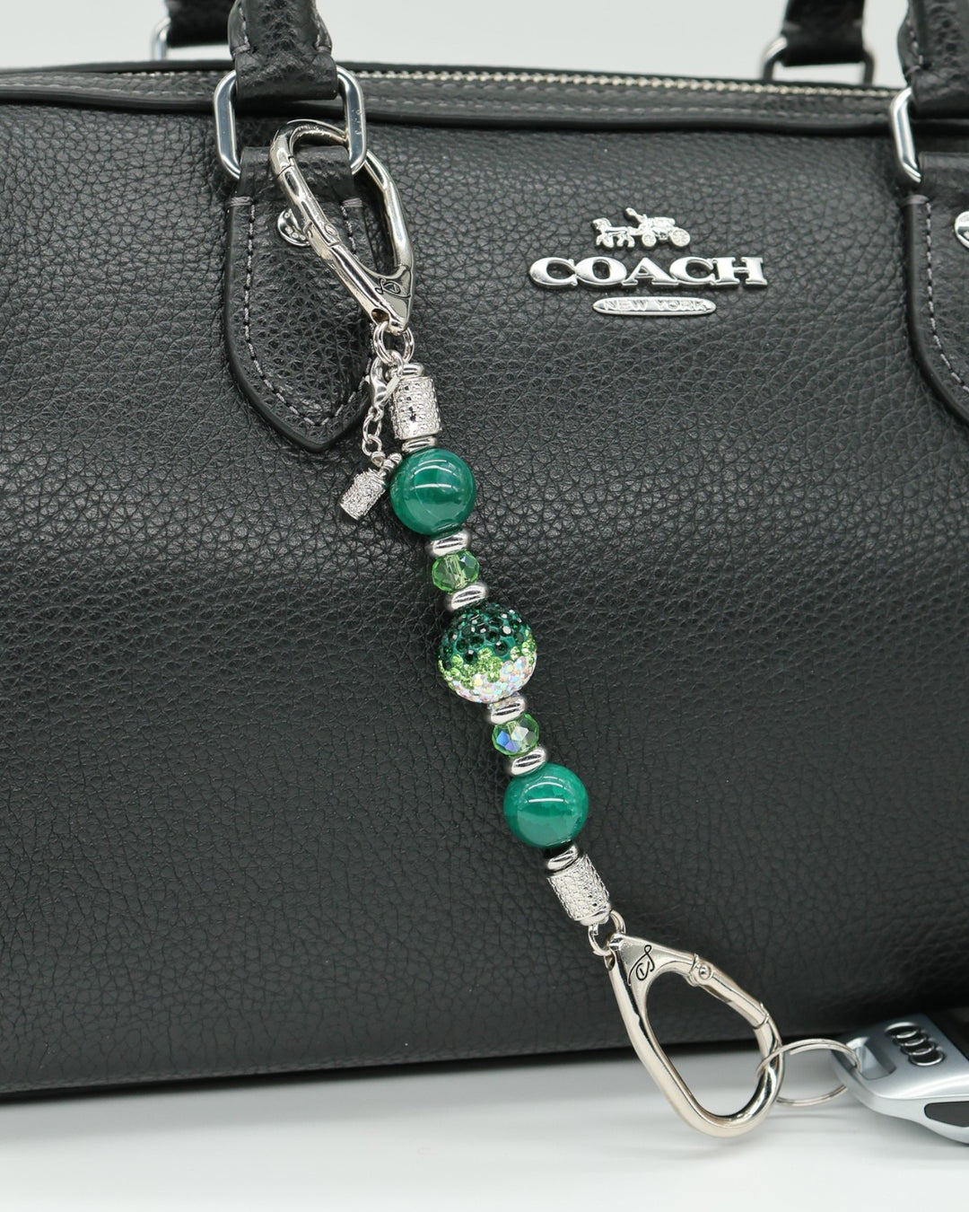 LD Keyfinder Emerald Links-Mini with green glass beads, Austrian crystal, and a golf bag charm on a black handbag.
