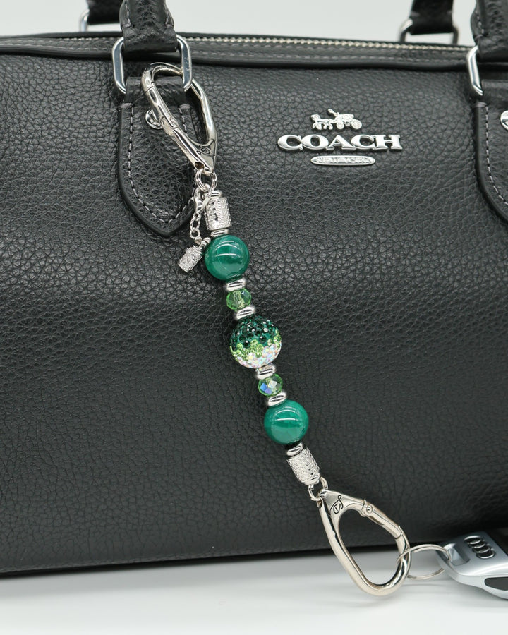 LD Keyfinder Emerald Links-Mini with green glass beads, Austrian crystal, and a golf bag charm on a black handbag.