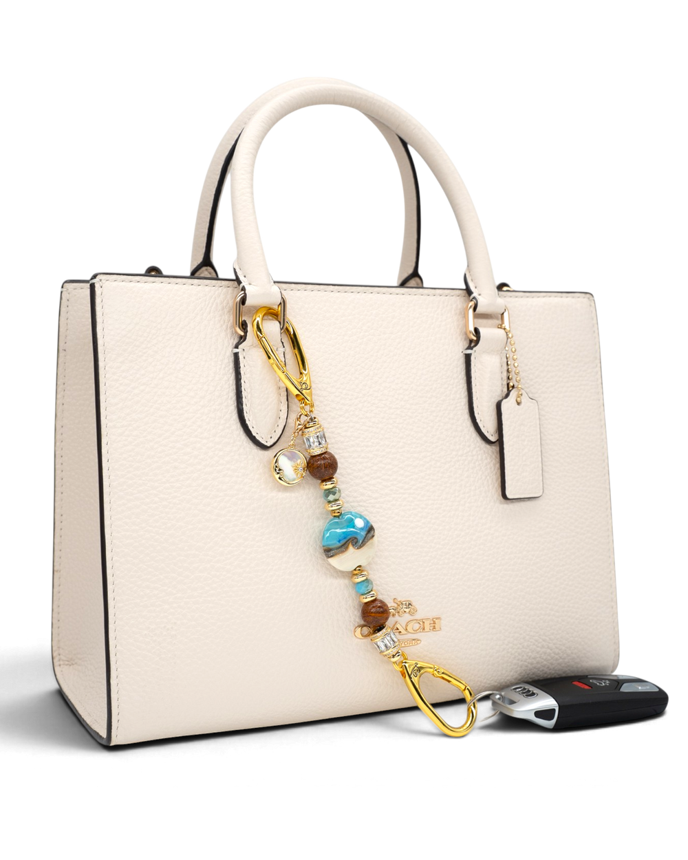 LD Keyfinder Petite Equinox Harmony beaded accessory with artisan glass, jasper, and gold charms on a cream handbag.