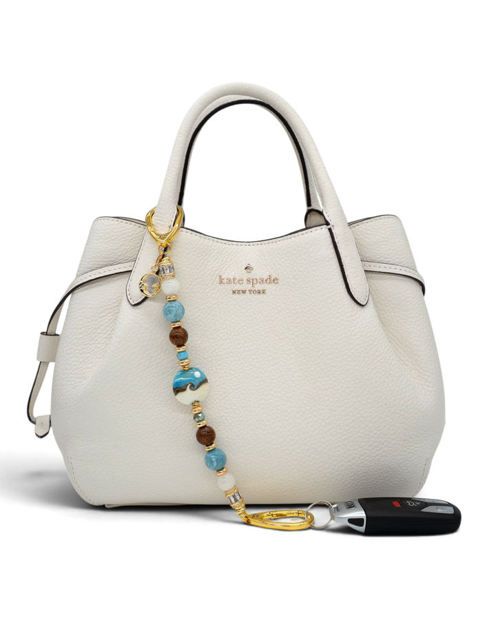 LD Keyfinder Equinox Harmony beaded accessory with moonstone, larimar, and artisan glass moon charm on a white handbag.