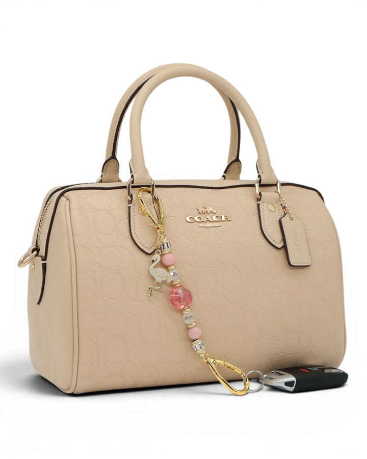 LD Keyfinder Petite Flamingo Fantasy accessory with pink opal beads and gold flamingo charm attached to a beige bag.