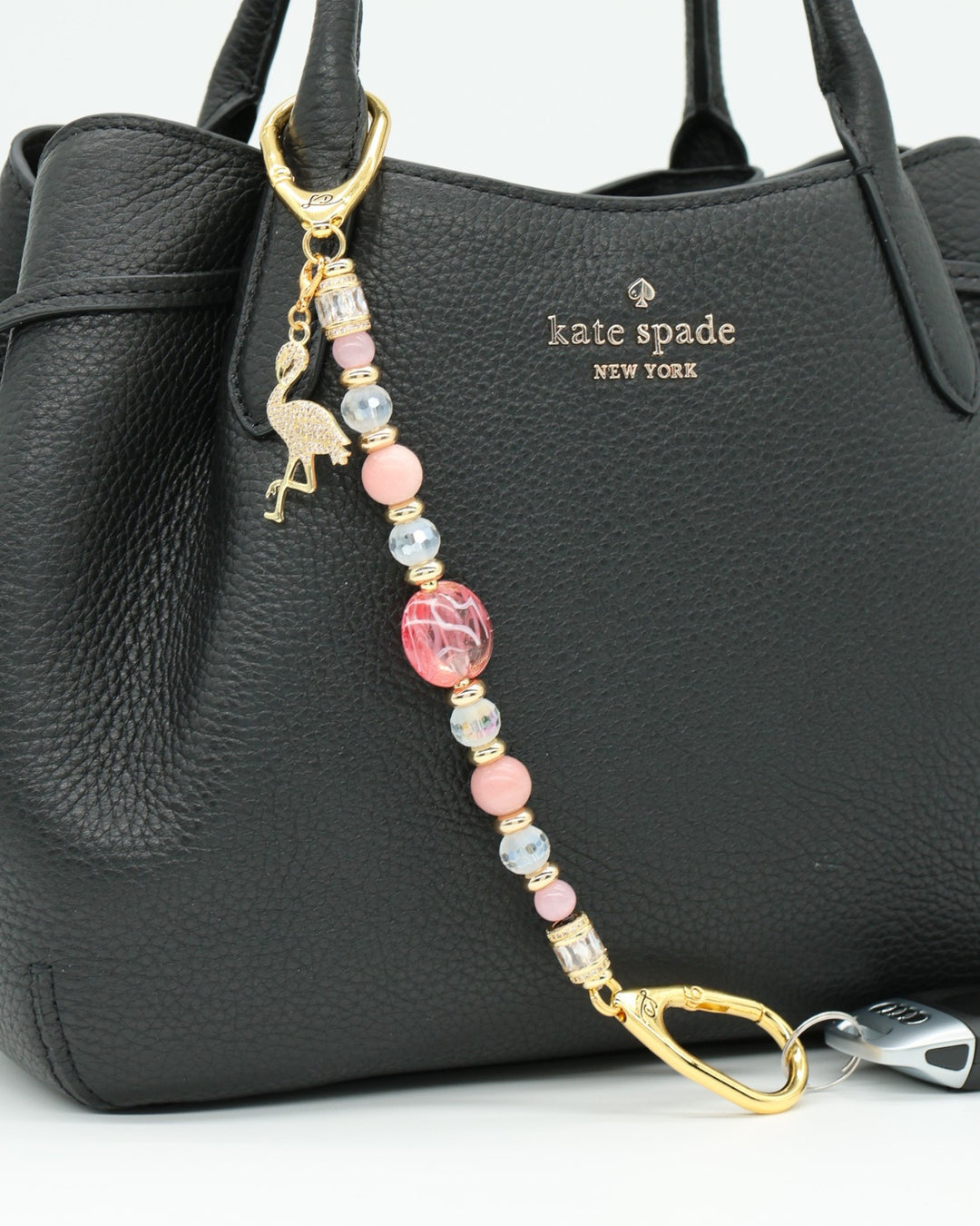 LD Keyfinder Flamingo Fantasy beaded accessory with pink opal, cat's eye beads, and a gold flamingo charm on a black bag.