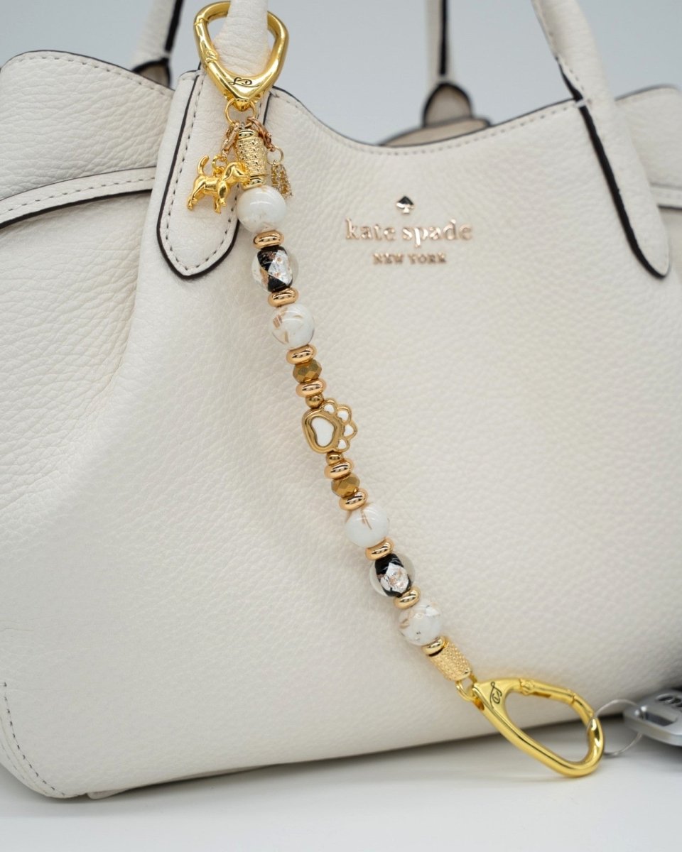 LD Keyfinder Furever Love beaded key chain with gold paw charm, white seashell beads, and gold accents on a white bag